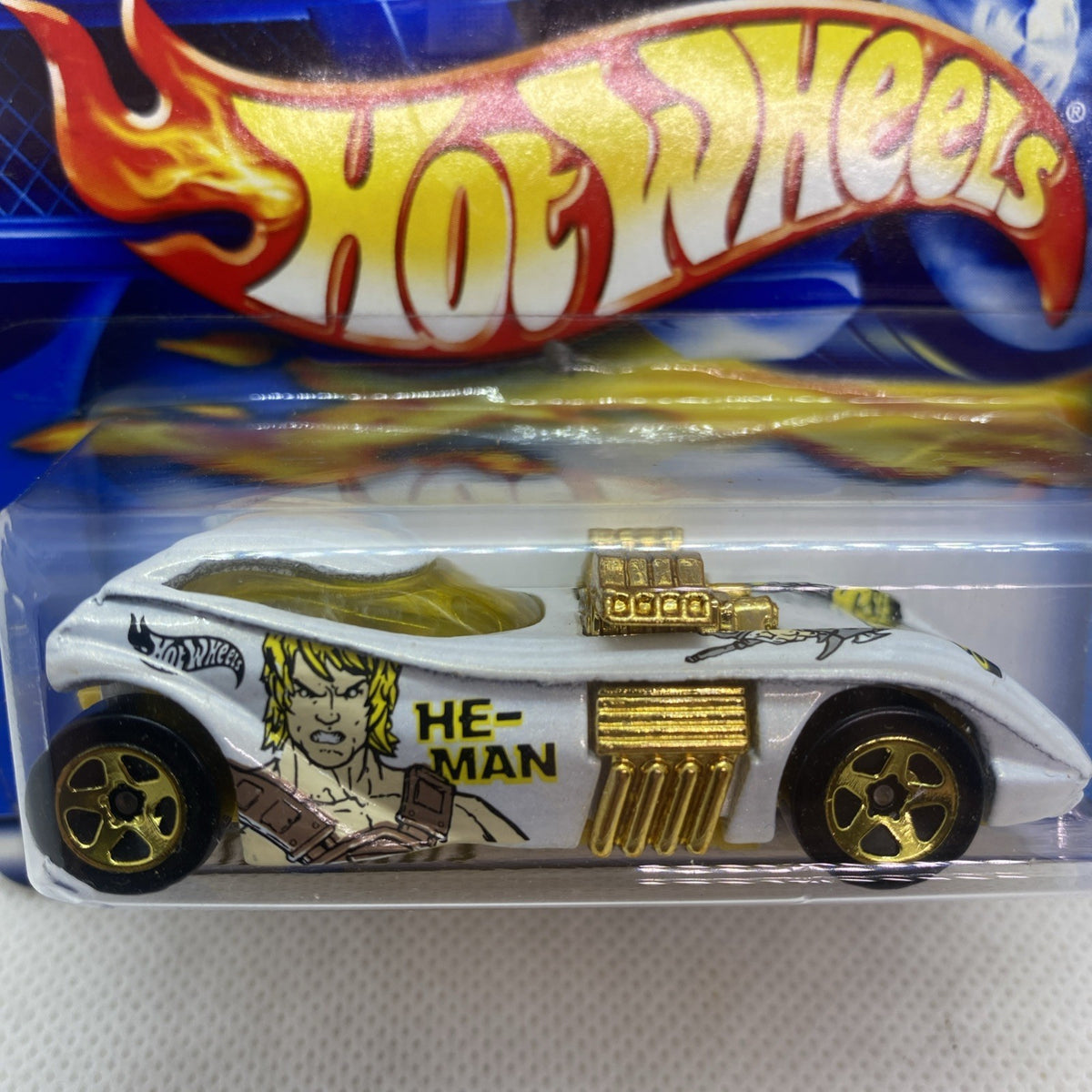 Hot Wheels die-cast car close-up in blister pack, white body, gold details, He-Man face art
