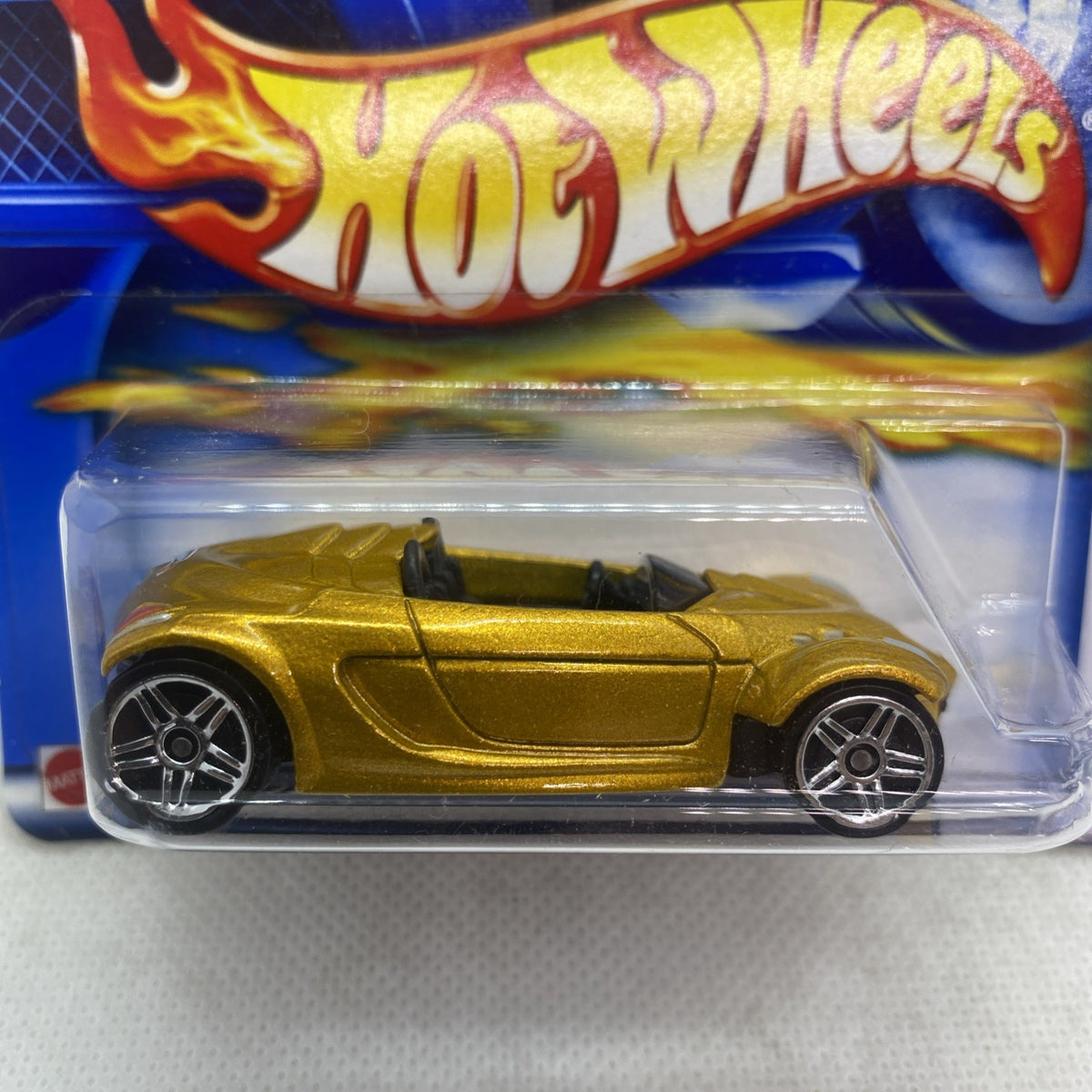 Hot Wheels gold die-cast car close-up in clear blister, front wheel visible