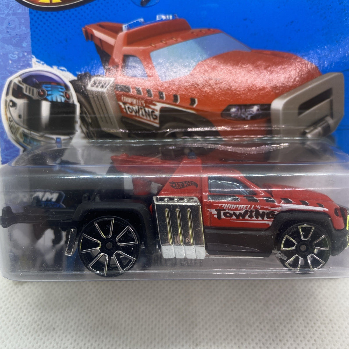 Close-up of red and orange die-cast tow truck in Hot Wheels blister, 1:64.