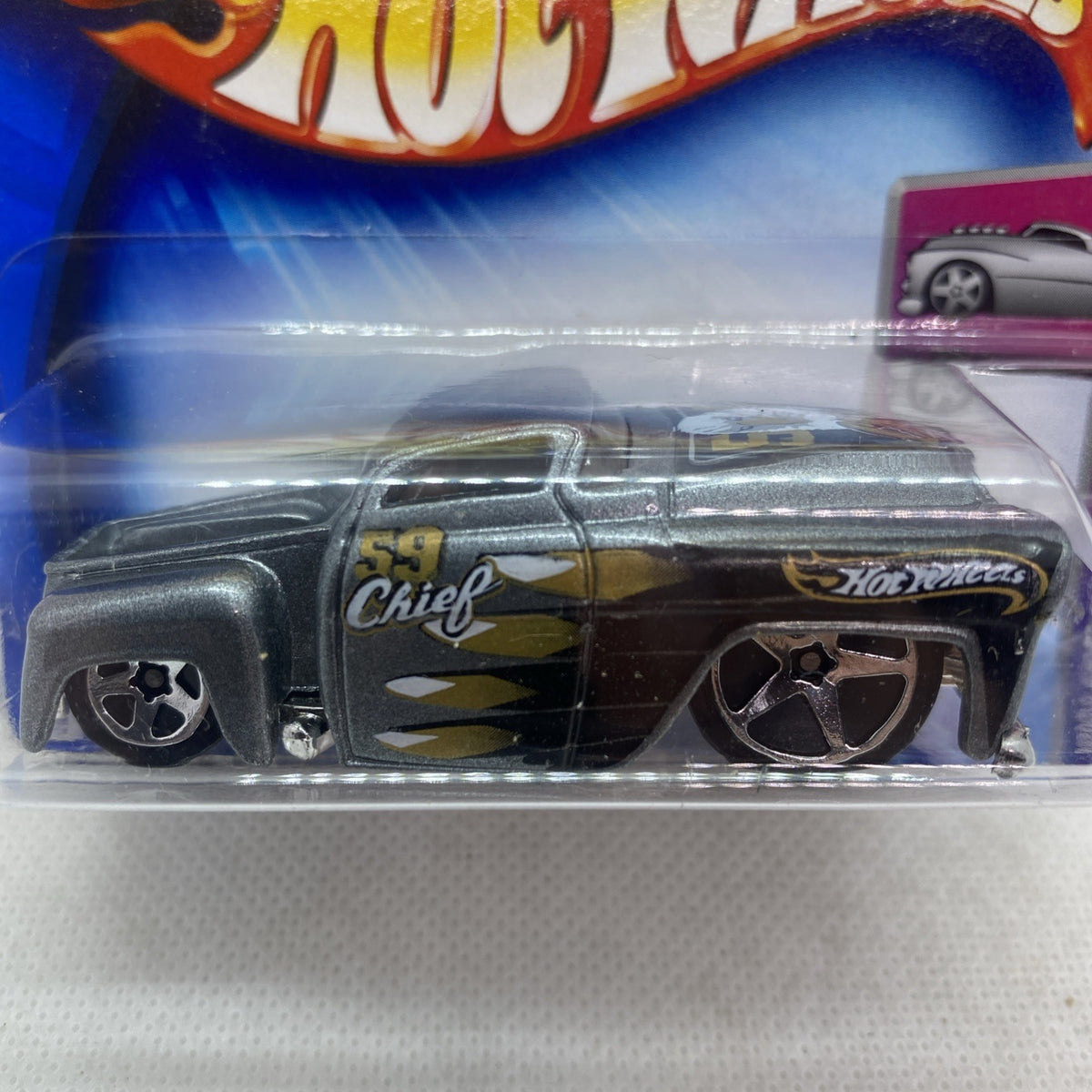 Close-up toy die-cast car in clear blister, dark gray body with gold stripe and emblem