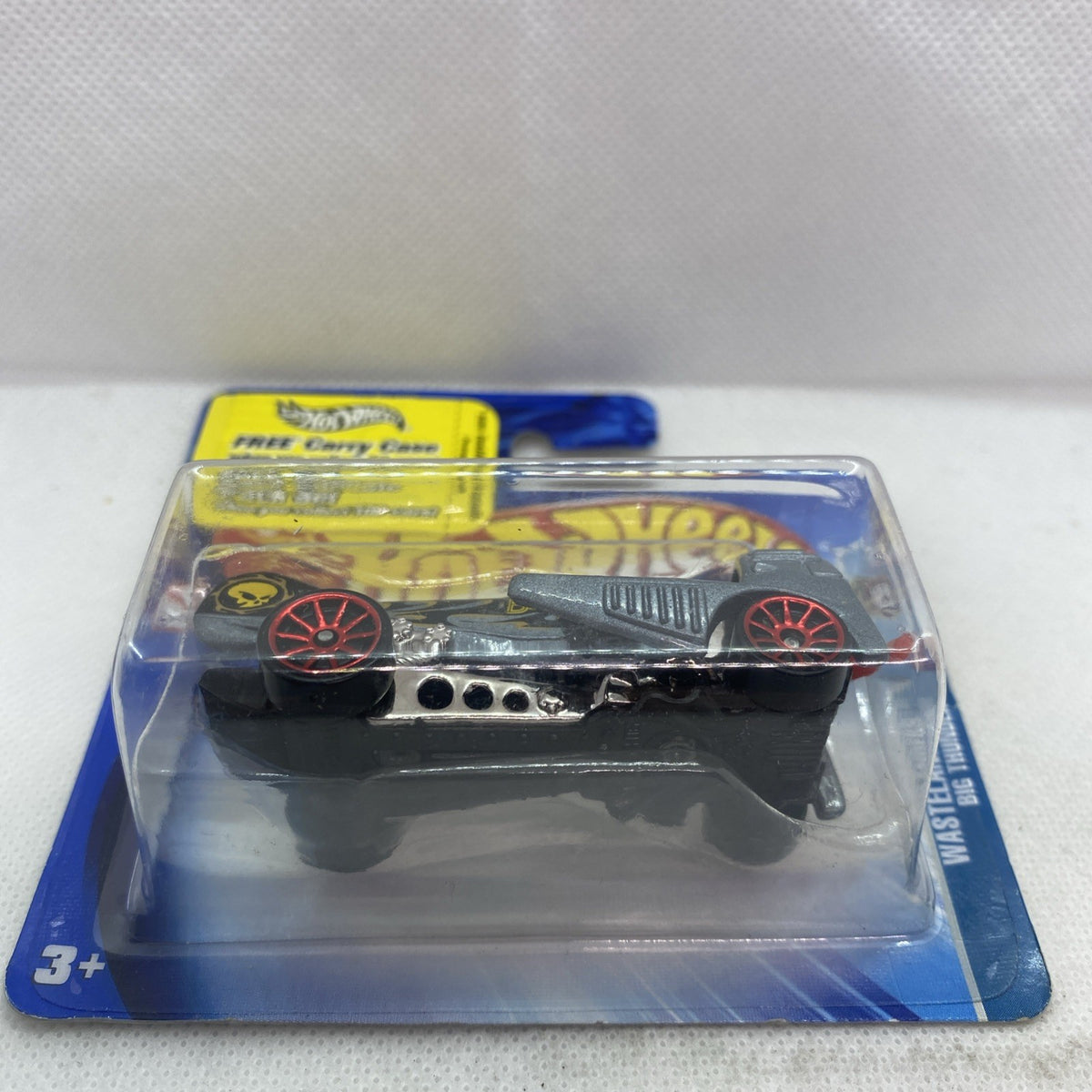 Hot Wheels die-cast truck in blister pack, close-up side view with red wheel rims