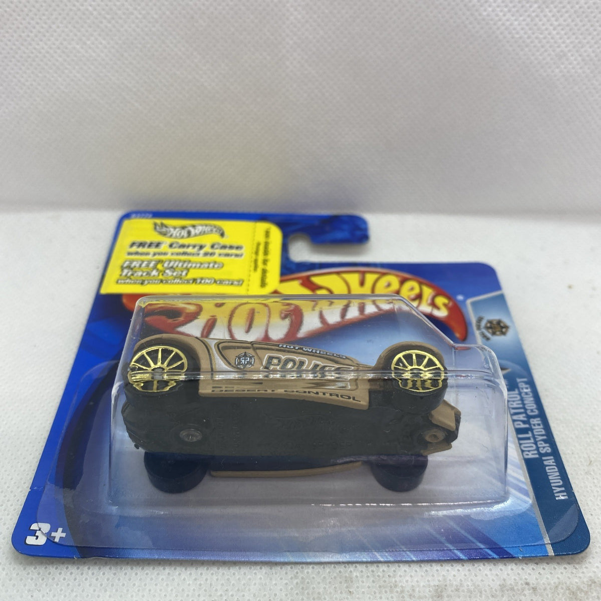 Beige Hot Wheels police die-cast car with black hood and gold wheels on retail card