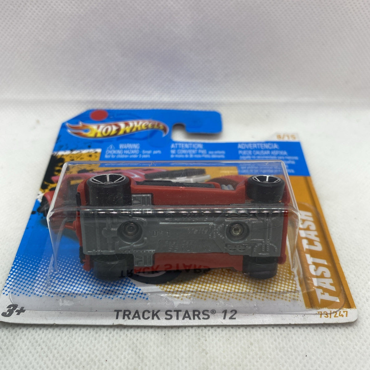 Hot Wheels diecast car underside view, red base with black wheels, sealed blister