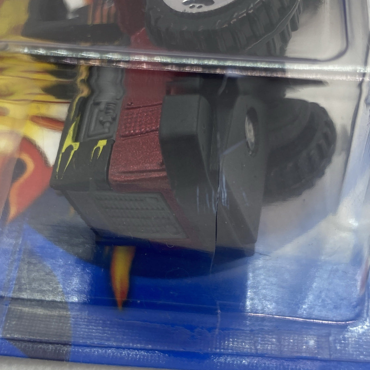 Close-up of red and black toy truck front details inside clear blister