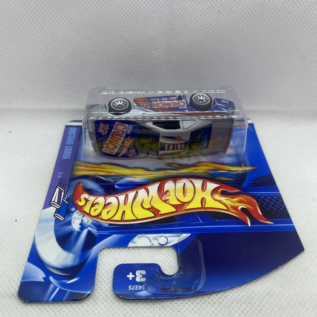 Hot Wheels sealed die-cast car on blue card with “Hot Wheels” flame logo and 3+ mark