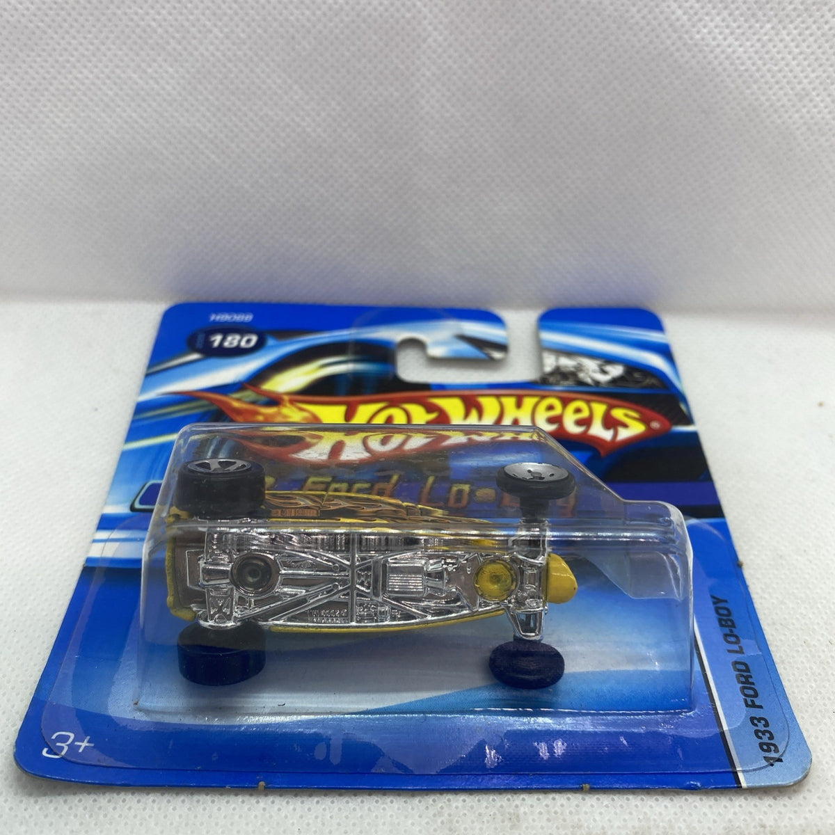 Yellow die-cast toy car in blister with detailed silver undercarriage and flame paint