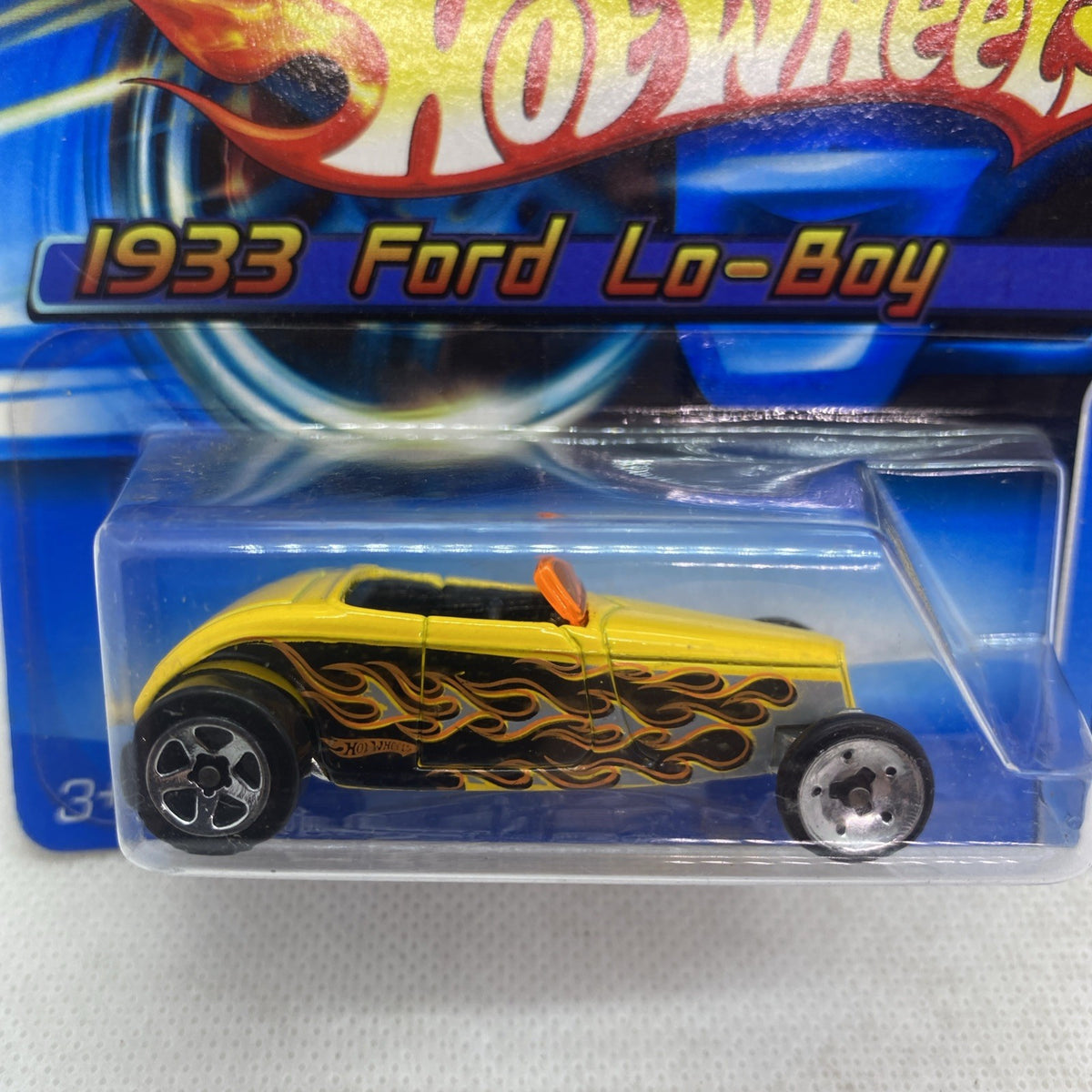 Close-up of a yellow die-cast toy car with black flame graphics, orange stripe, silver wheels