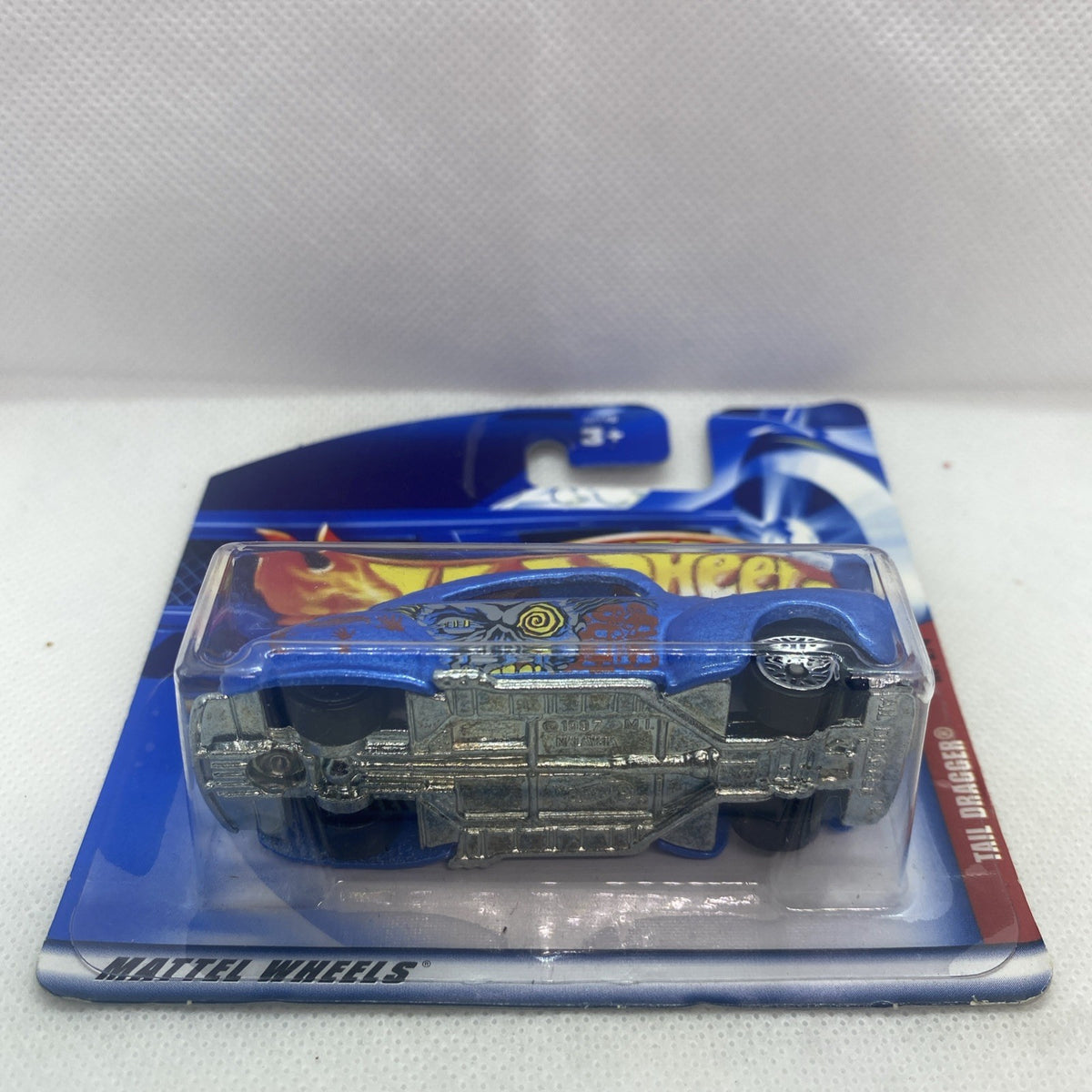 Hot Wheels blue tail-dragger die-cast car in sealed blister card, bottom details visible.