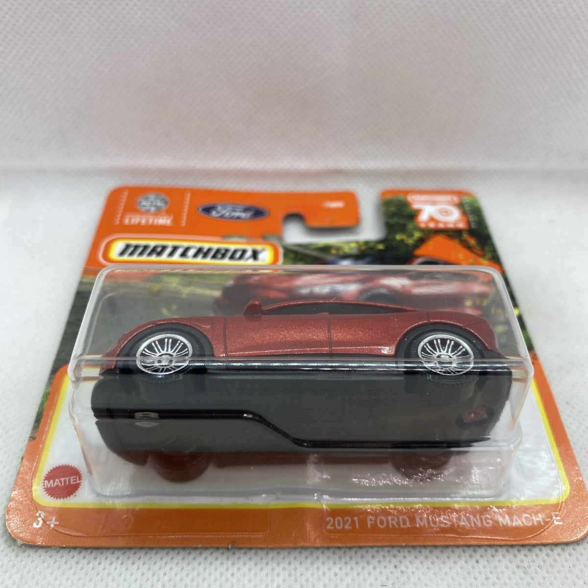 Red-brown die-cast toy car in clear blister on orange Matchbox card, side view