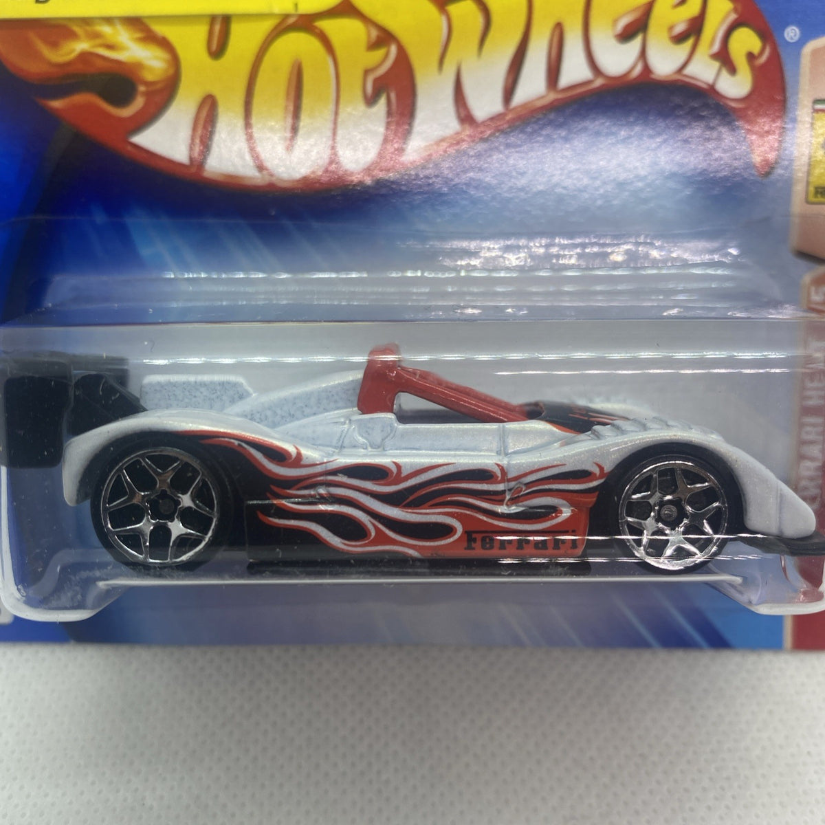 Close-up of die-cast race car: white body, red flame stripes, black multi-spoke wheels