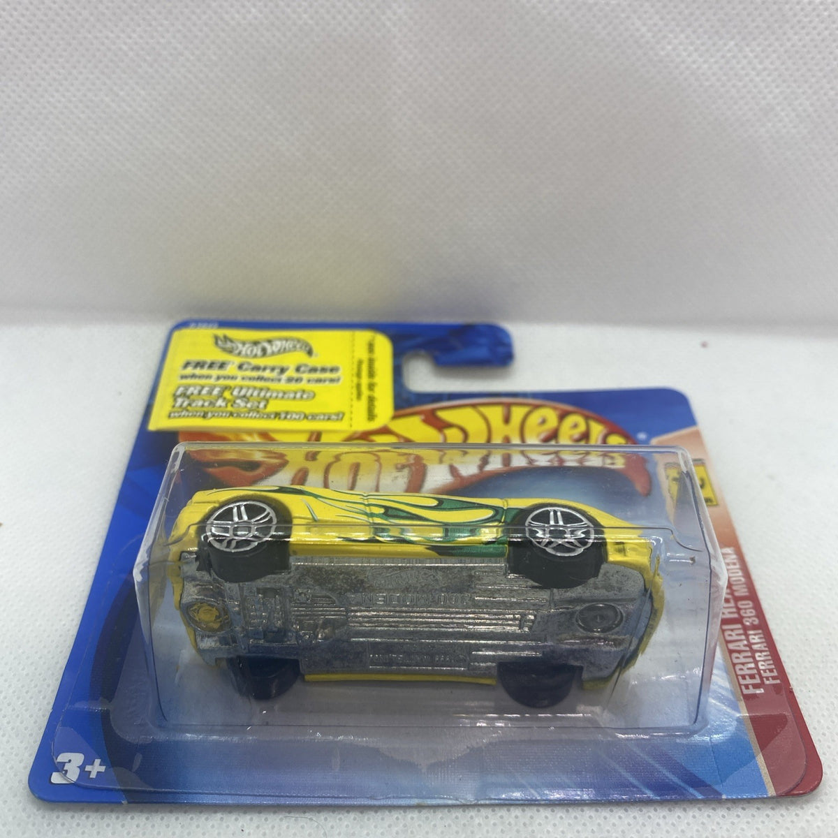 Yellow die-cast car in blister pack viewed from above, showing black wheels