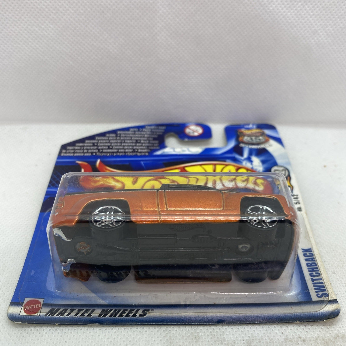 Hot Wheels die-cast car in blister, side view with orange body and black base in package.