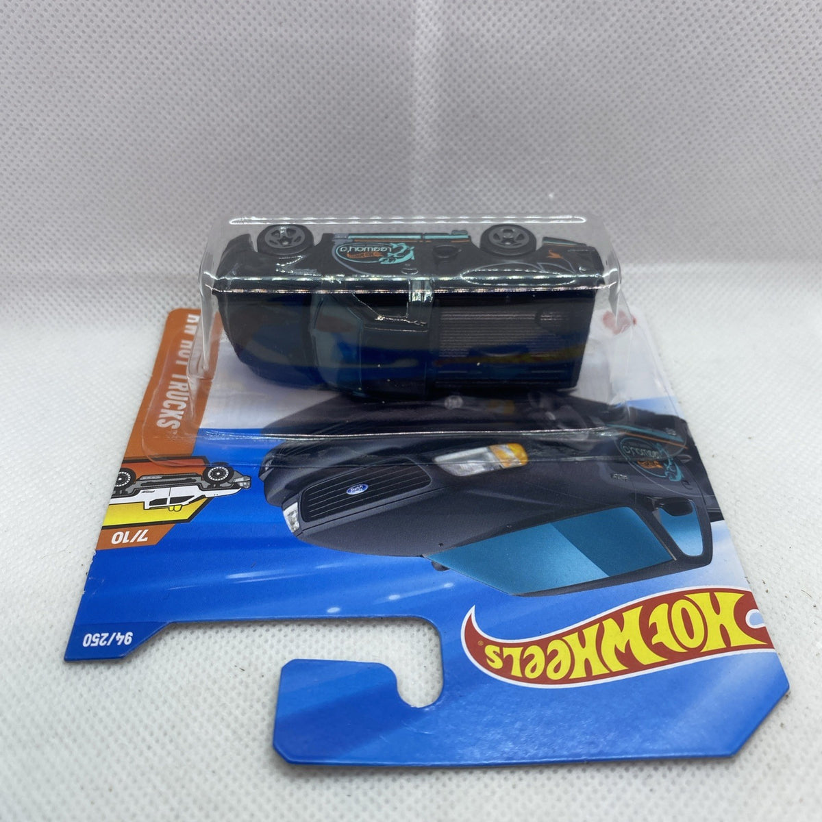 Hot Wheels toy pickup truck in blister, dark body with teal decals, front and side view.