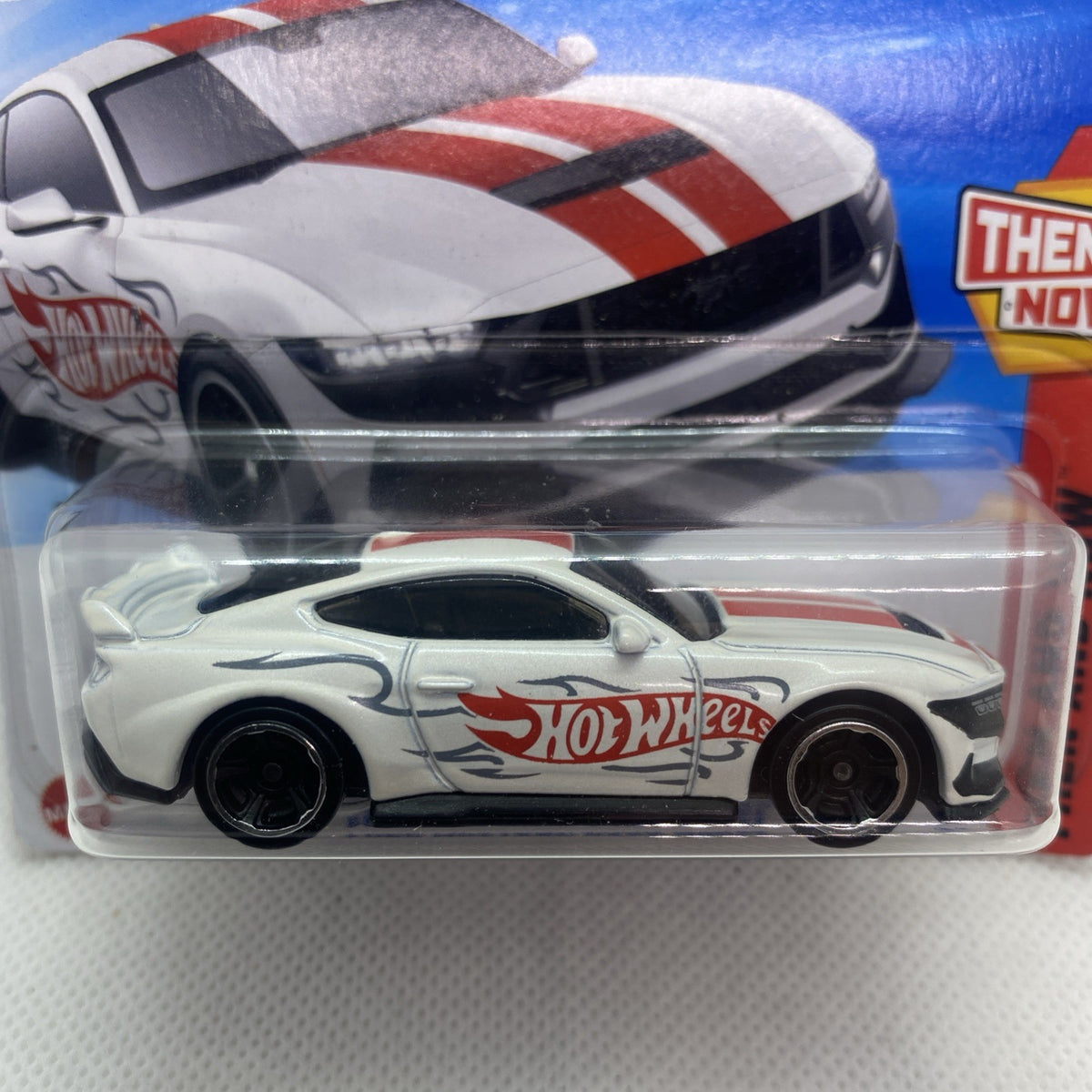 Hot Wheels toy car blister close-up: white body, red stripes, black wheels