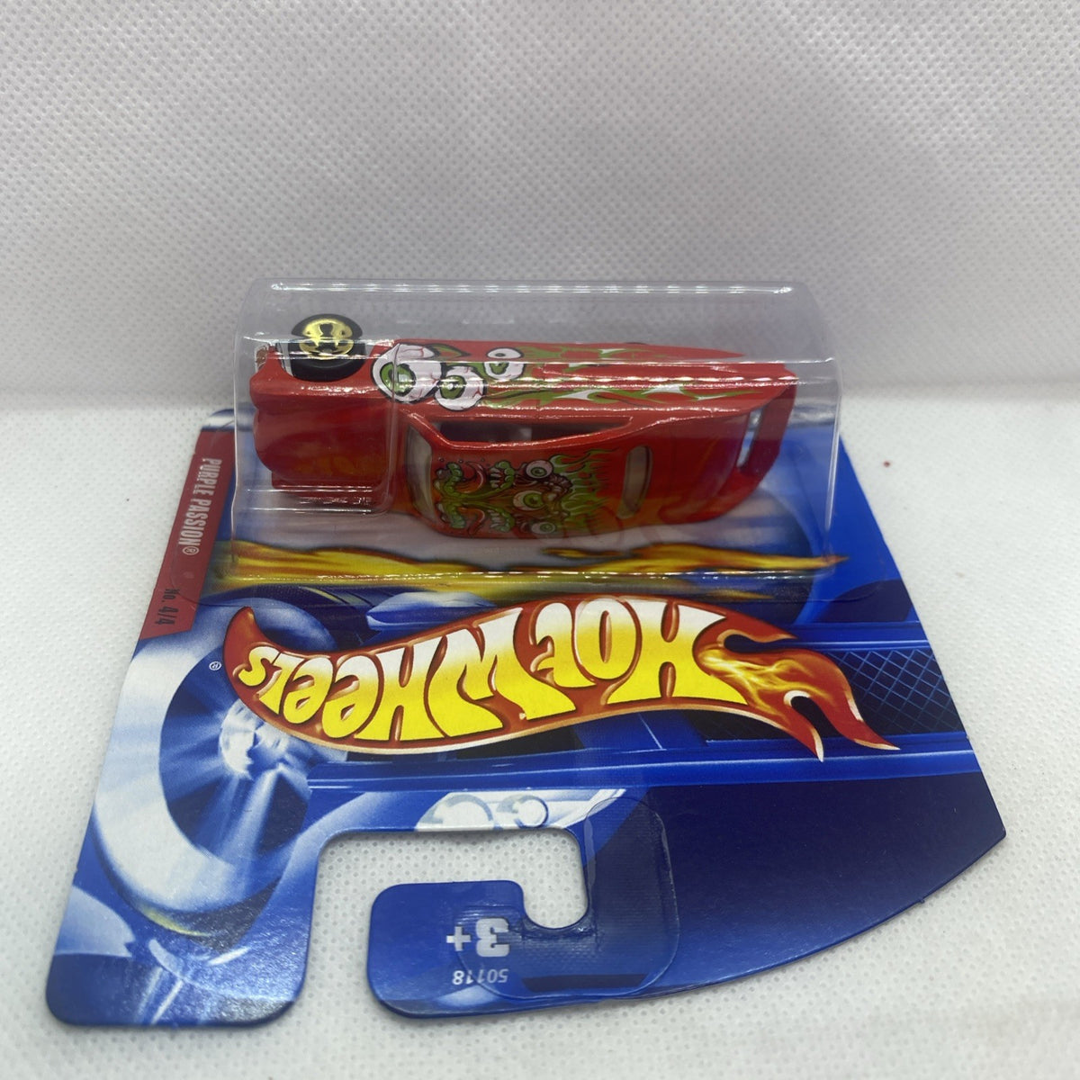 Hot Wheels blister toy car on blue card, red body with green flame monster decals, gold wheels