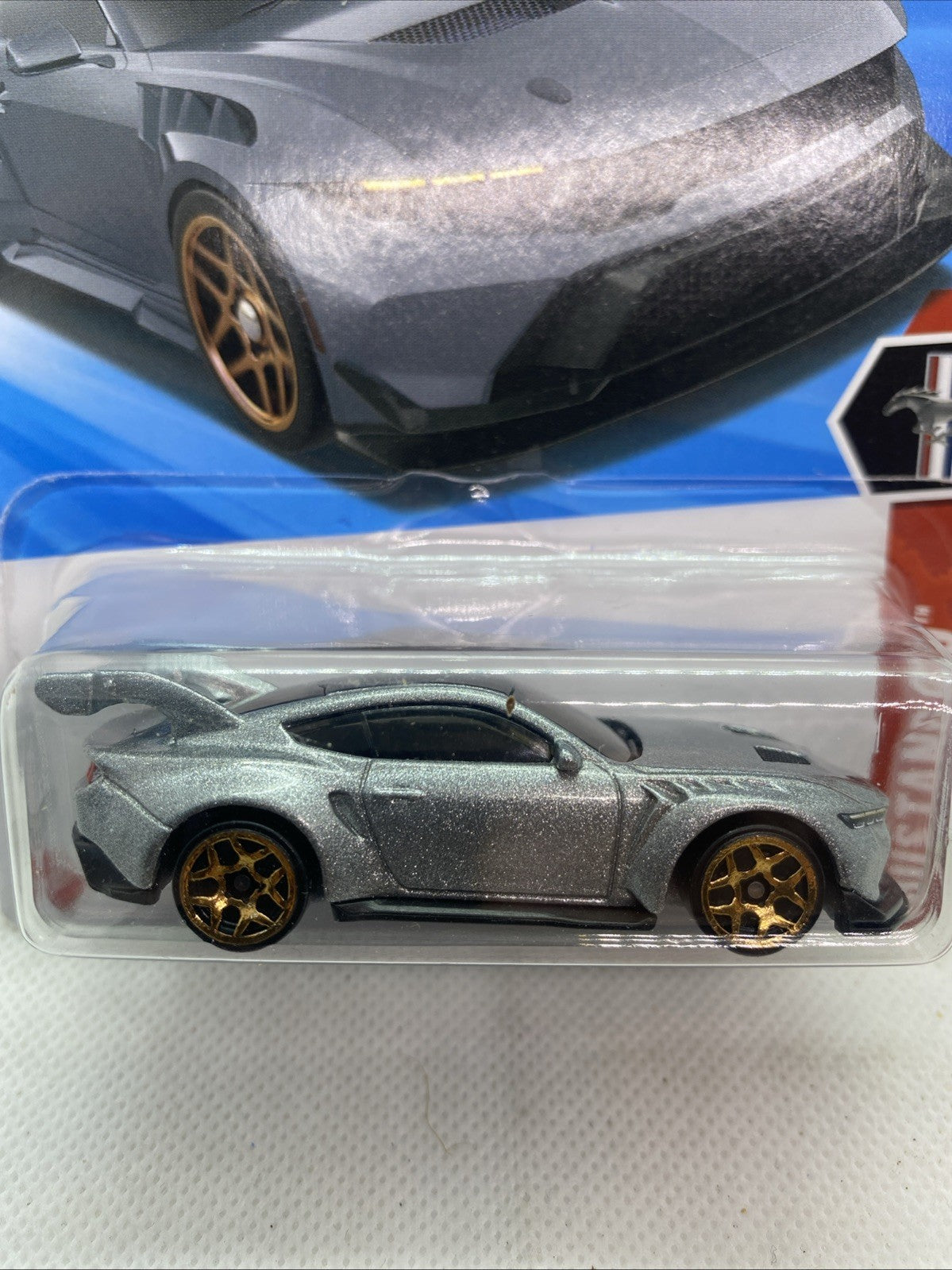 Close-up Hot Wheels Ford Mustang GTD die-cast on card, silver-gray with gold wheels