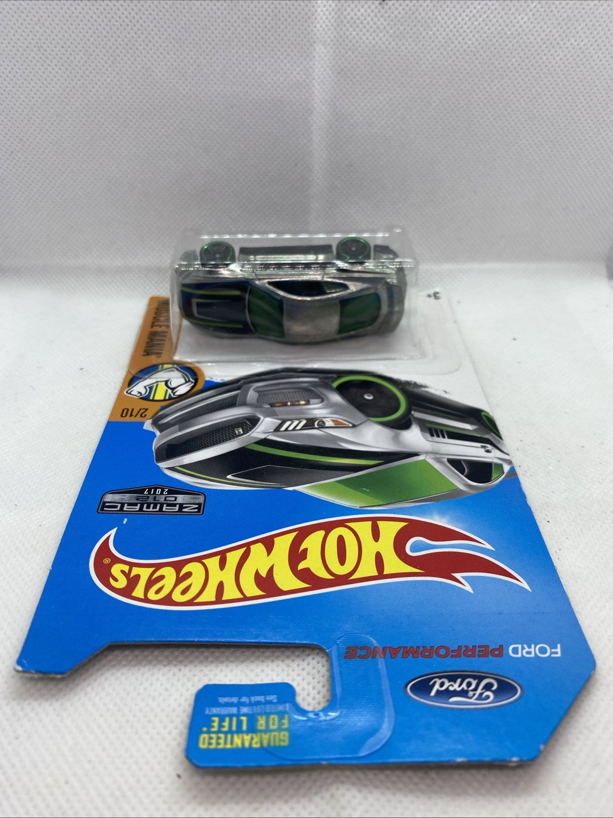 Hot Wheels die-cast muscle car lying on blue card backing, green wheel accents