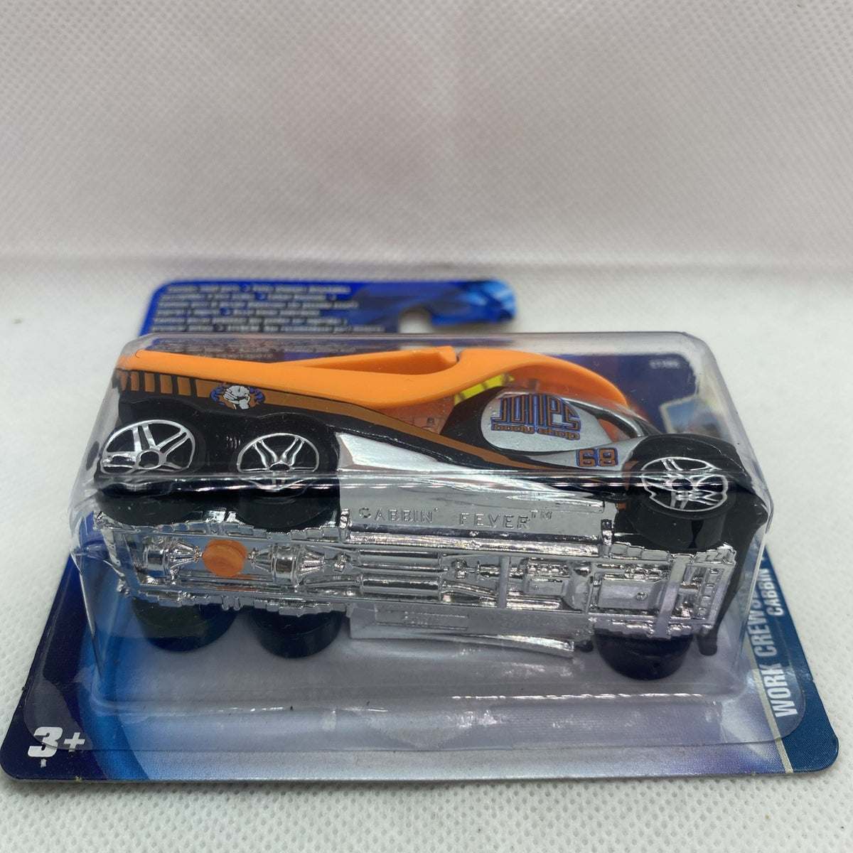 Hot Wheels die-cast toy car in clear blister, orange and black with exposed engine, side view.