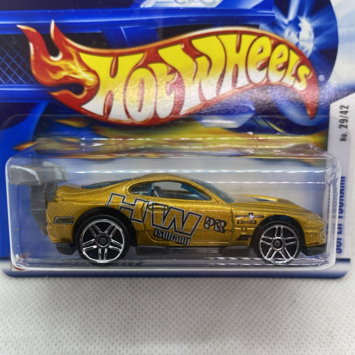 Hot Wheels Super Tsunami die-cast car close-up in sealed blister, gold body and flame graphics