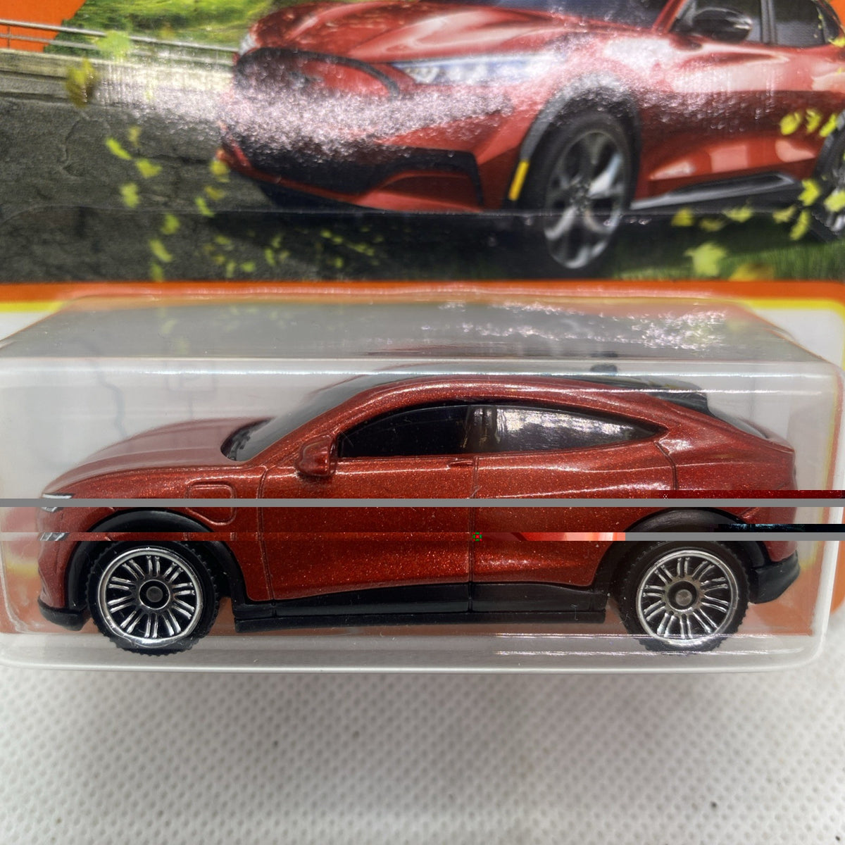Close-up of red-brown die-cast toy car in clear blister with black wheels and windows
